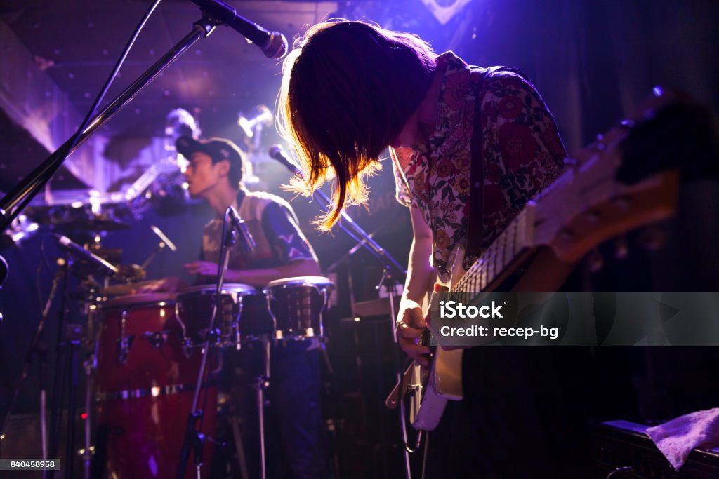 a young japanese woman is playing the guitar during a live band event.
